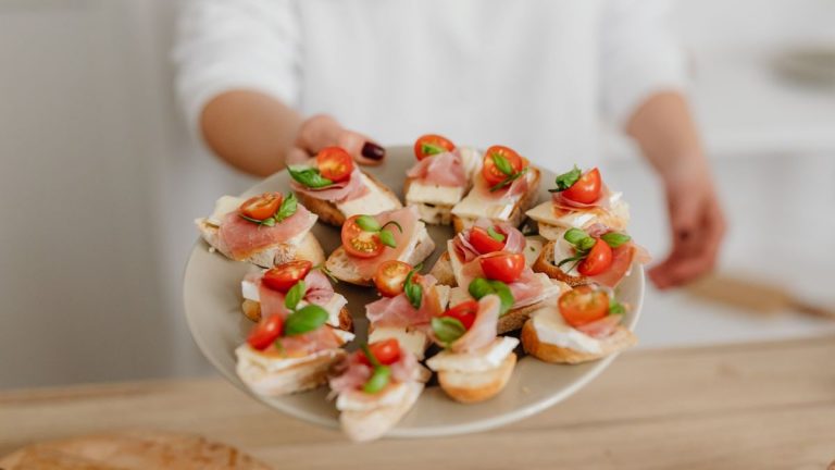 Close-up of a plate with canapés topped with prosciutto, cheese, and cherry tomatoes.